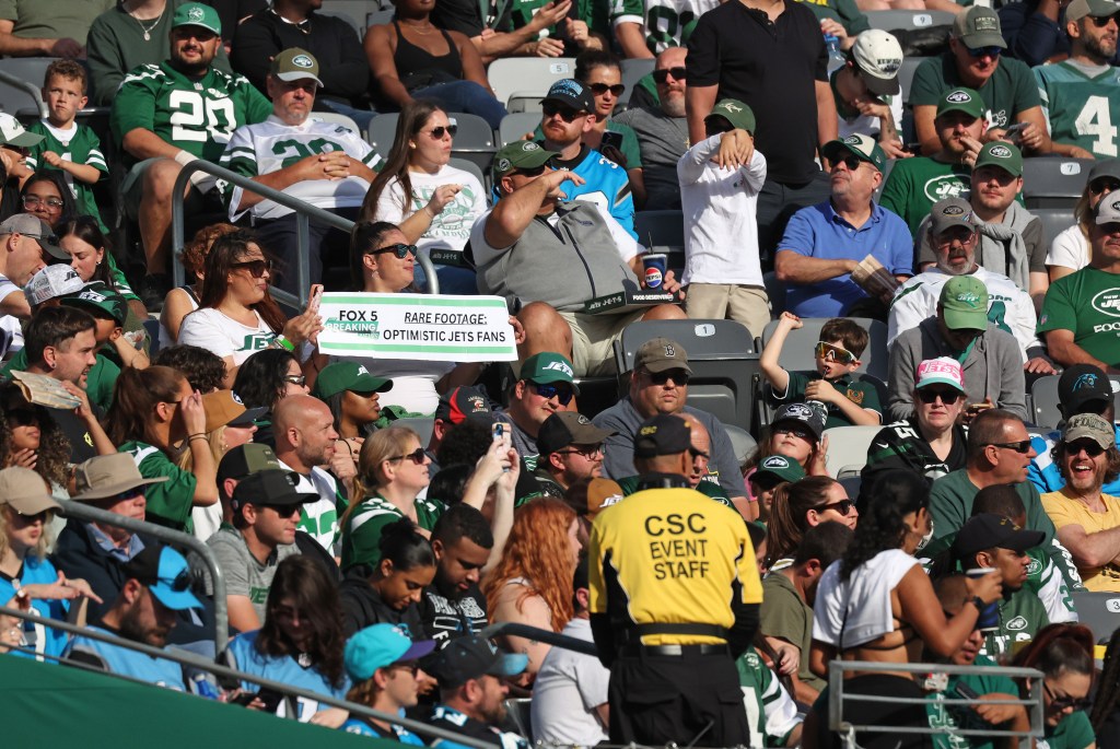 New York Jets fans in the stands, with one fan holding a sign that reads "Rare Footage: Optimistic Jets Fans."
