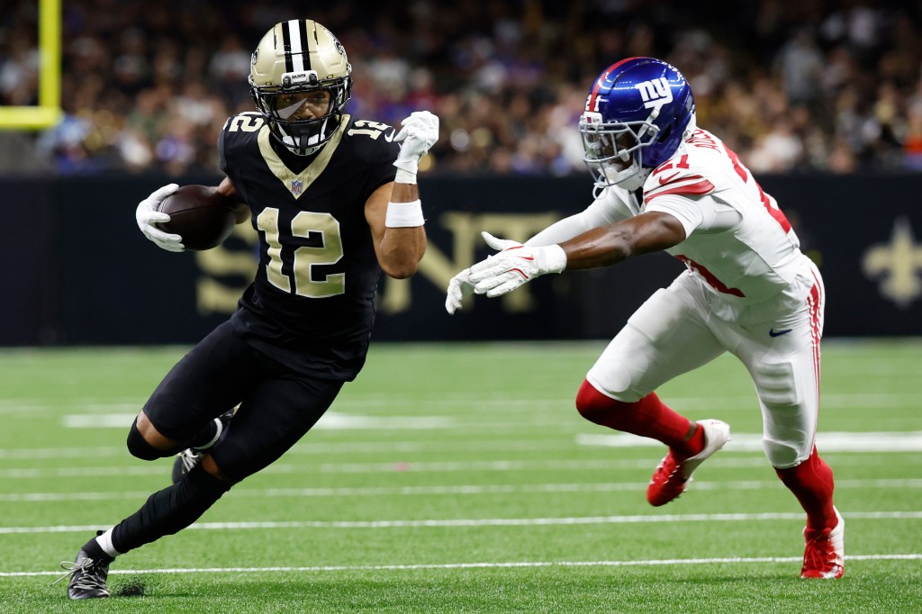 New Orleans Saints wide receiver Chris Olave runs with the ball while New York Giants cornerback Paulson Adebo pursues him during a football game.