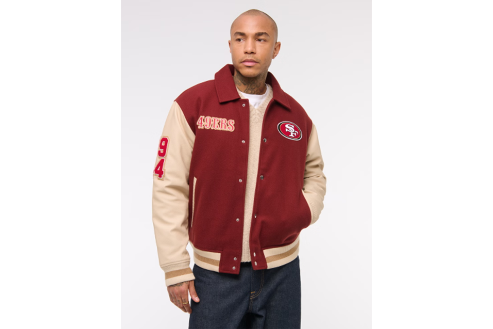 A man wearing a red and beige San Francisco 49ers varsity jacket with "49ERS" and "94" embroidered on it.
