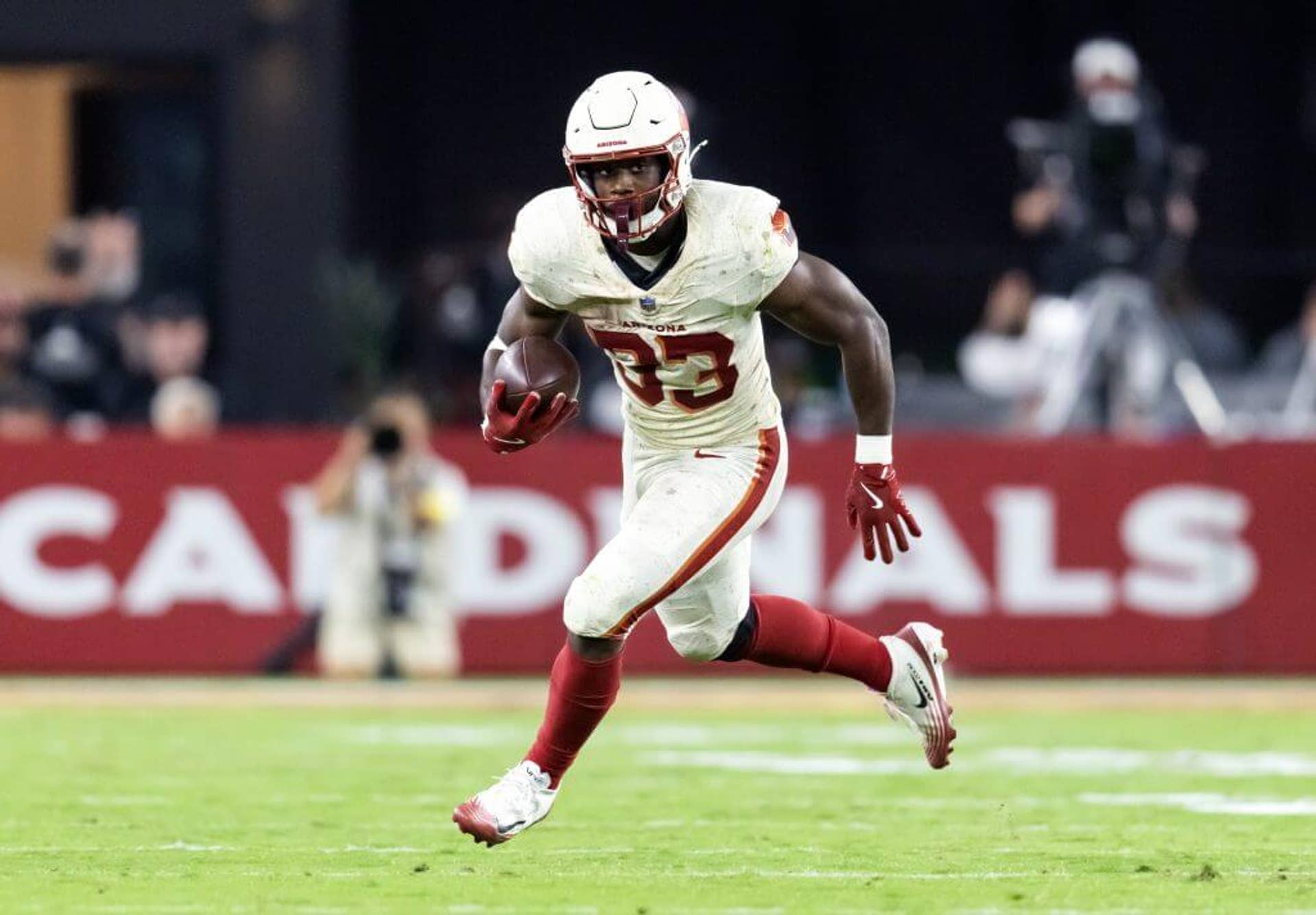 Arizona running back Trey Benson, wearing a while helmet, jersey and pants, strides in the open field with the ball tucked into his right side.