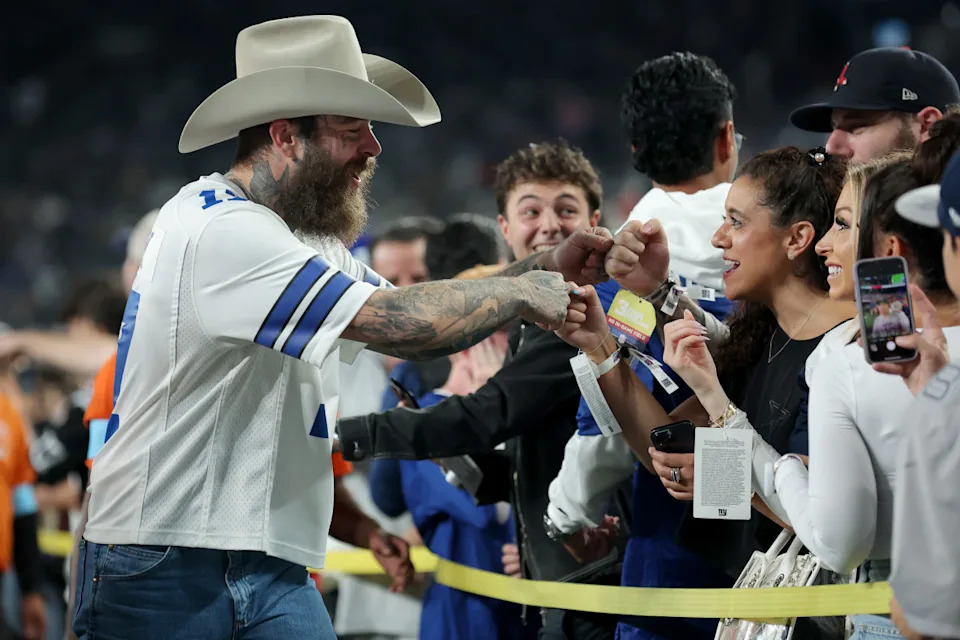 Sep 26, 2024; East Rutherford, New Jersey, USA; American recording artist Post Malone (left) fist bumps fans on the field before a game between the New York Giants and the Dallas Cowboys at MetLife Stadium. Mandatory Credit: Brad Penner-Imagn Images© Brad Penner-Imagn Images
