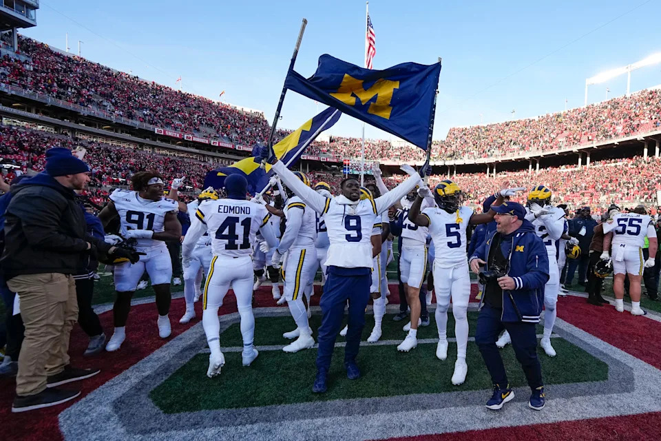 Michigan Wolverines players celebrate at midfield just before pretending to plant a flag on the field.