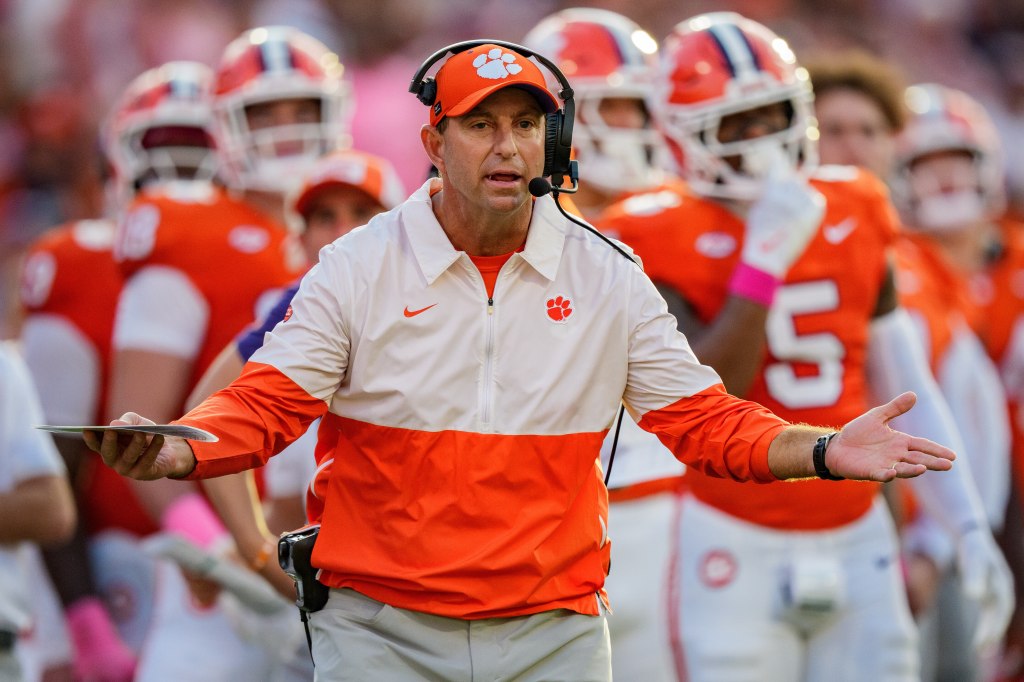 Clemson football coach Dabo Swinney on the sidelines with players in the background.