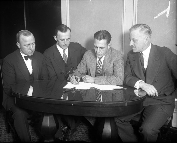 On Nov. 22, 1925, less than 24 hours after his last game with the Fighting Illini, Harold "Red" Grange, second from right, signed a contract to play pro football with the Chicago Bears at the Morrison Hotel in Chicago. Surrounding Grange as he signed were Bears managers Edward C. Sternaman, from left, and George C. Halas. Grange's agent Charles C. Pyle, is on the right. (Chicago Herald and Examiner photo)