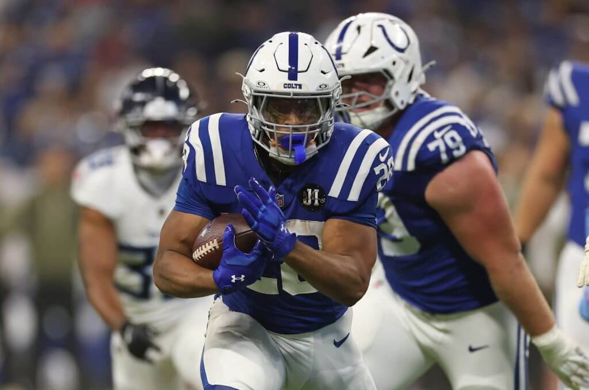 Jonathan Taylor in a blue jersey holding the ball to his left with both arms.