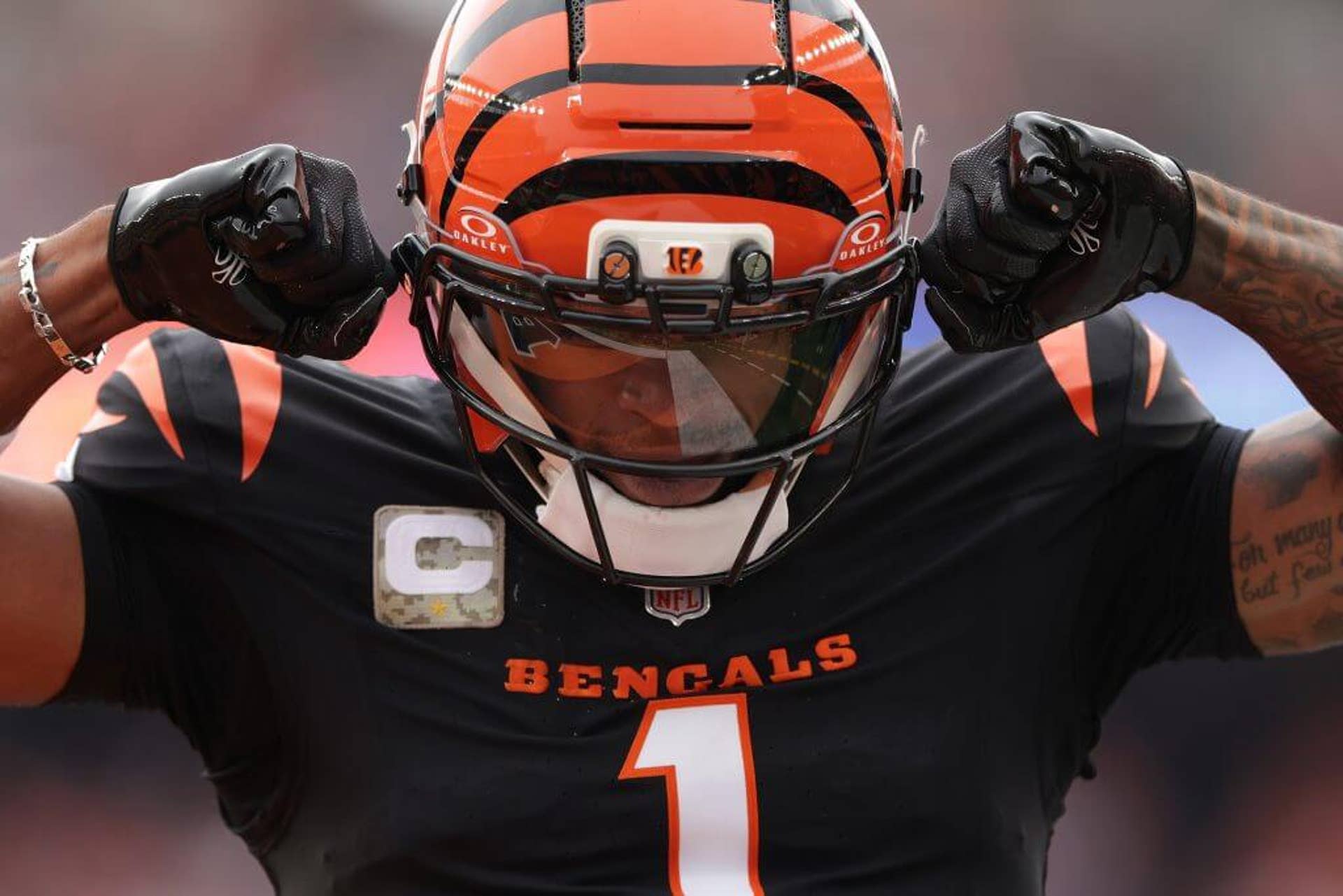 Ja'Marr Chase, clad in a black uniform and orange helmet with black stripes, flexes his muscles.