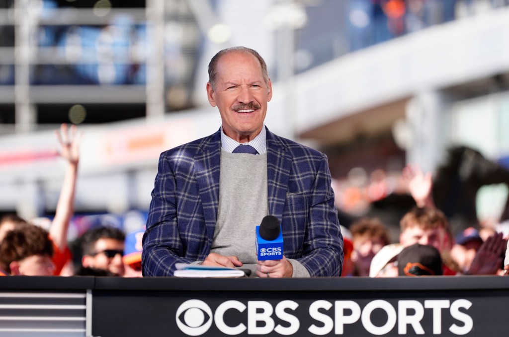 CBS Sports broadcaster Bill Cowher smiling behind a desk with a microphone.