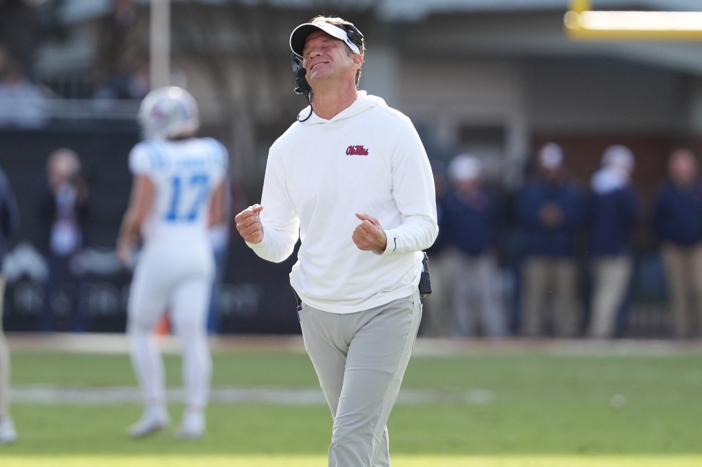 Lane Kiffin, wearing a white visor and white sweatshirt with "Ole Miss" in red on the chest, reacts to an official's call during a football game.