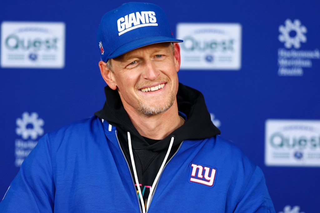 New York Giants defensive coordinator Charlie Bullen smiles while wearing a blue Giants hat and jacket during football practice.
