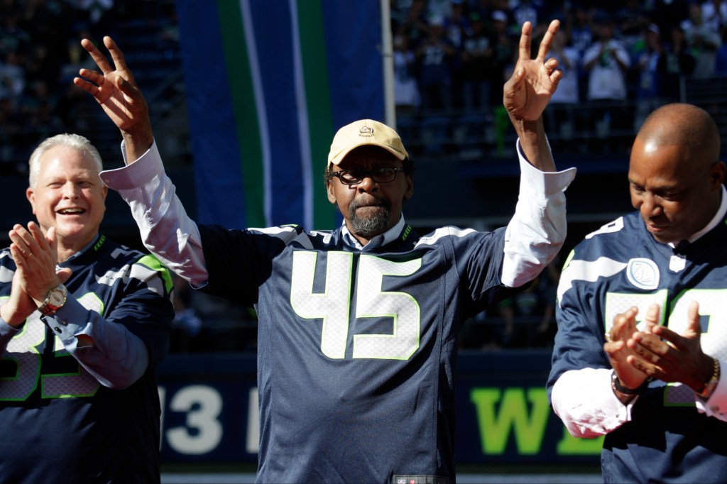 Kenny Easley, wearing a Seattle Seahawks jersey with the number 45, raises his arms in celebration.