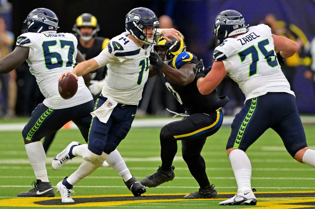 Seattle Seahawks quarterback Sam Darnold (14) runs away from Los Angeles Rams linebacker Byron Young (0) during a game.
