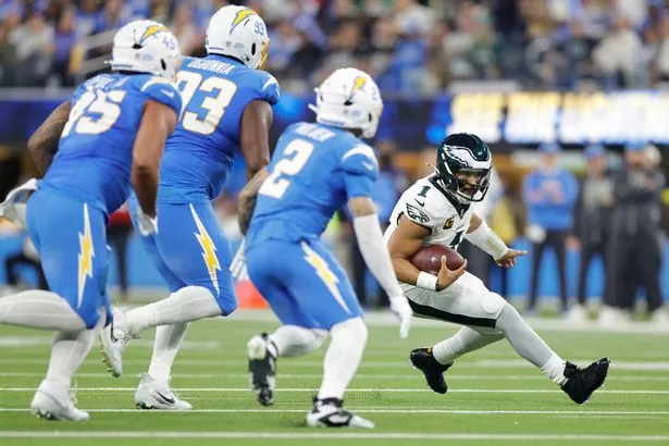 Jalen Hurts being chased by several Chargers defenders