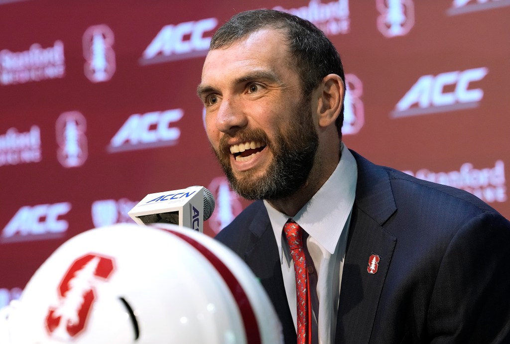 Tavita Pritchard smiling at a press conference, with a microphone and Stanford helmet in the foreground.