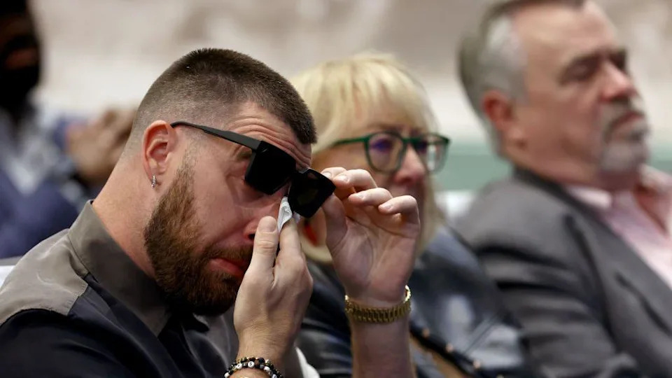 Travis Kelce of the Kansas City Chiefs wipes his eyes during his brother Jason's retirement from the NFL in March 2024, sat next to their mother and father