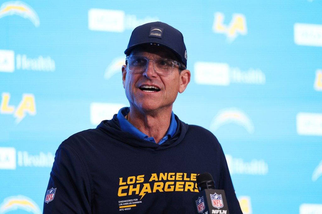 Jim Harbaugh of the Los Angeles Chargers wearing a cap and sweatshirt with team logos.
