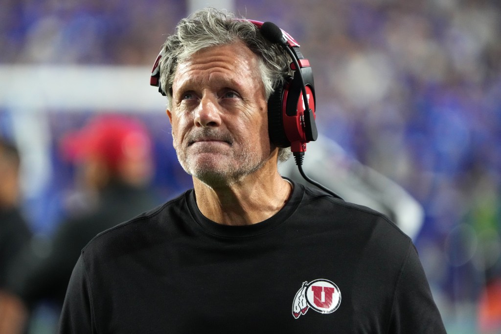 A football coach wearing a black shirt with a red Ute logo and red headphones.