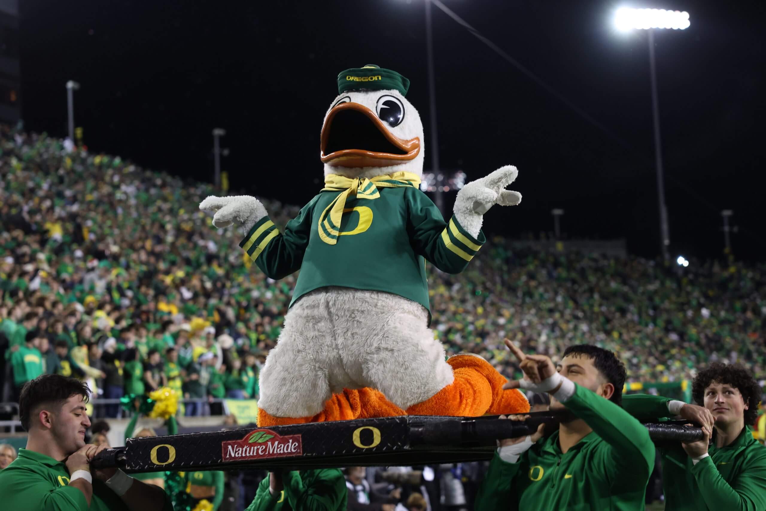 The Oregon Duck mascot kneels on a platform and signals to the crowd