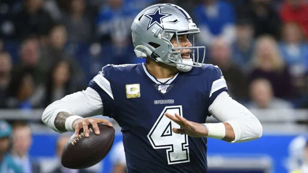 1. Dallas Cowboys quarterback Dak Prescott in action during an NFL game, wearing team uniform and helmet, holding football ready to throw, on the field with blurred fans in background.