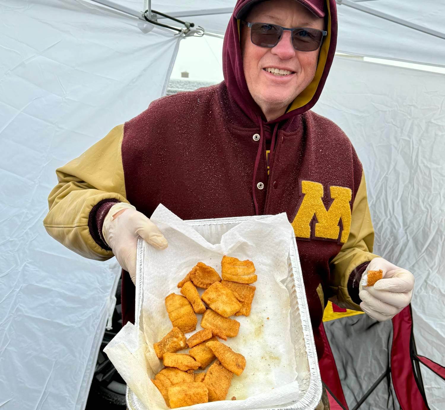 Minnesota football fan Mike Piel holds up a platter of his fried walleye at a tailgate.
