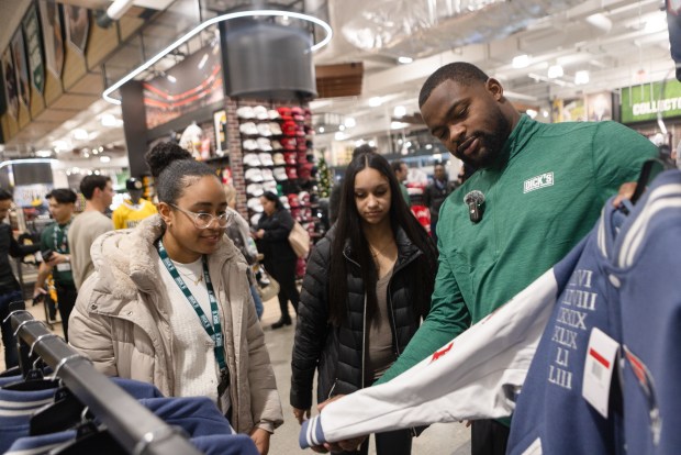 Boston's Aneyli Tejeda (left), Janelly Sanchez, and Patriots wide receiver Kayshon Boutte admire a Patriots letterman's jacket during a holiday shopping event at DICK'S House of Sport Boston. (Libby O'Neill/Boston Herald)