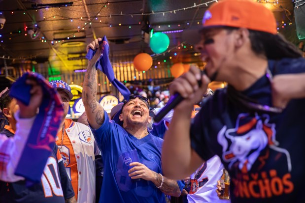 Original Bronco Gang member Ray Gurule, center, cheers as Andrew Young, The Mad Fanatic, right, performs at The Point Sports Bar and Grill in Thornton on Saturday, Nov. 15, 2025. (Photo by McKenzie Lange/Special to The Denver Post)
