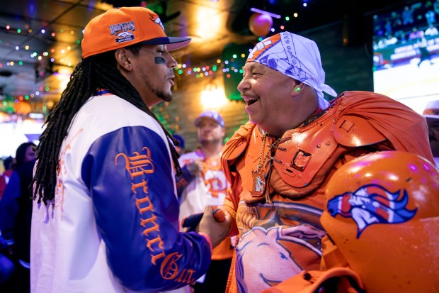 Andrew Young, The Mad Fanatic, left, congratulates Bronco Gang member James Chavez, known as Orange Vader, after winning a raffle prize at The Point Sports Bar and Grill in Thornton on Saturday, Nov. 15, 2025. (Photo by McKenzie Lange/Special to The Denver Post)