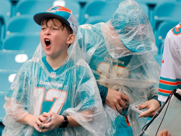 Miami Dolphins fans in rain gear ask for autographs before...