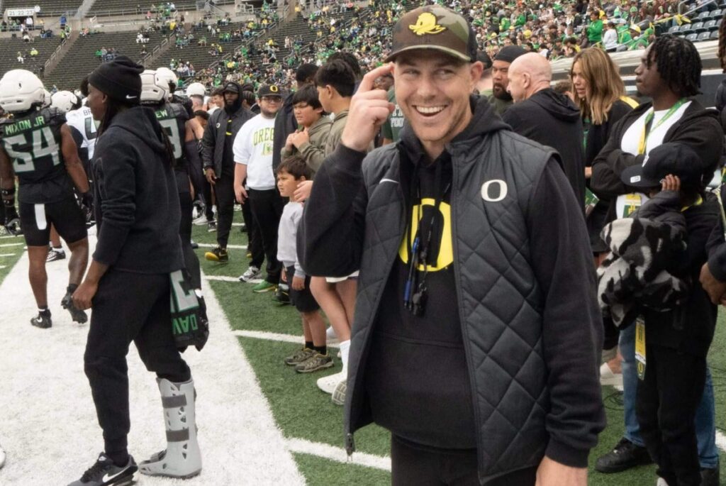 Will Stein on the sidelines of an Oregon game, smiling.