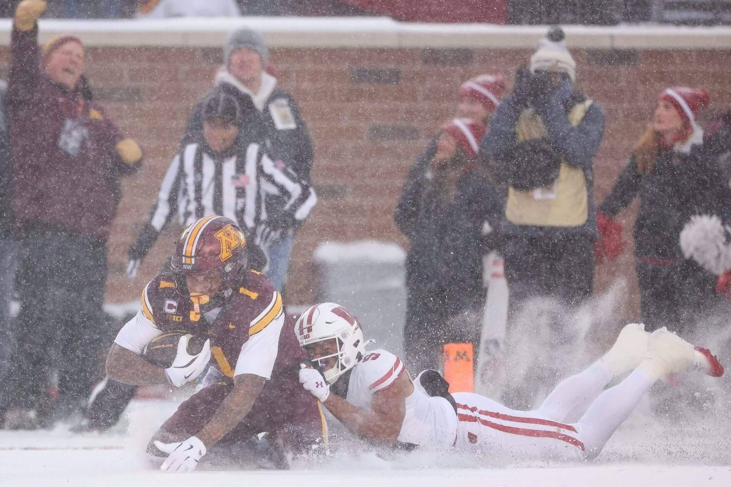 Minnesota running back Darius Taylor slides in the snow as he's tackled by a Wisconsin defender.