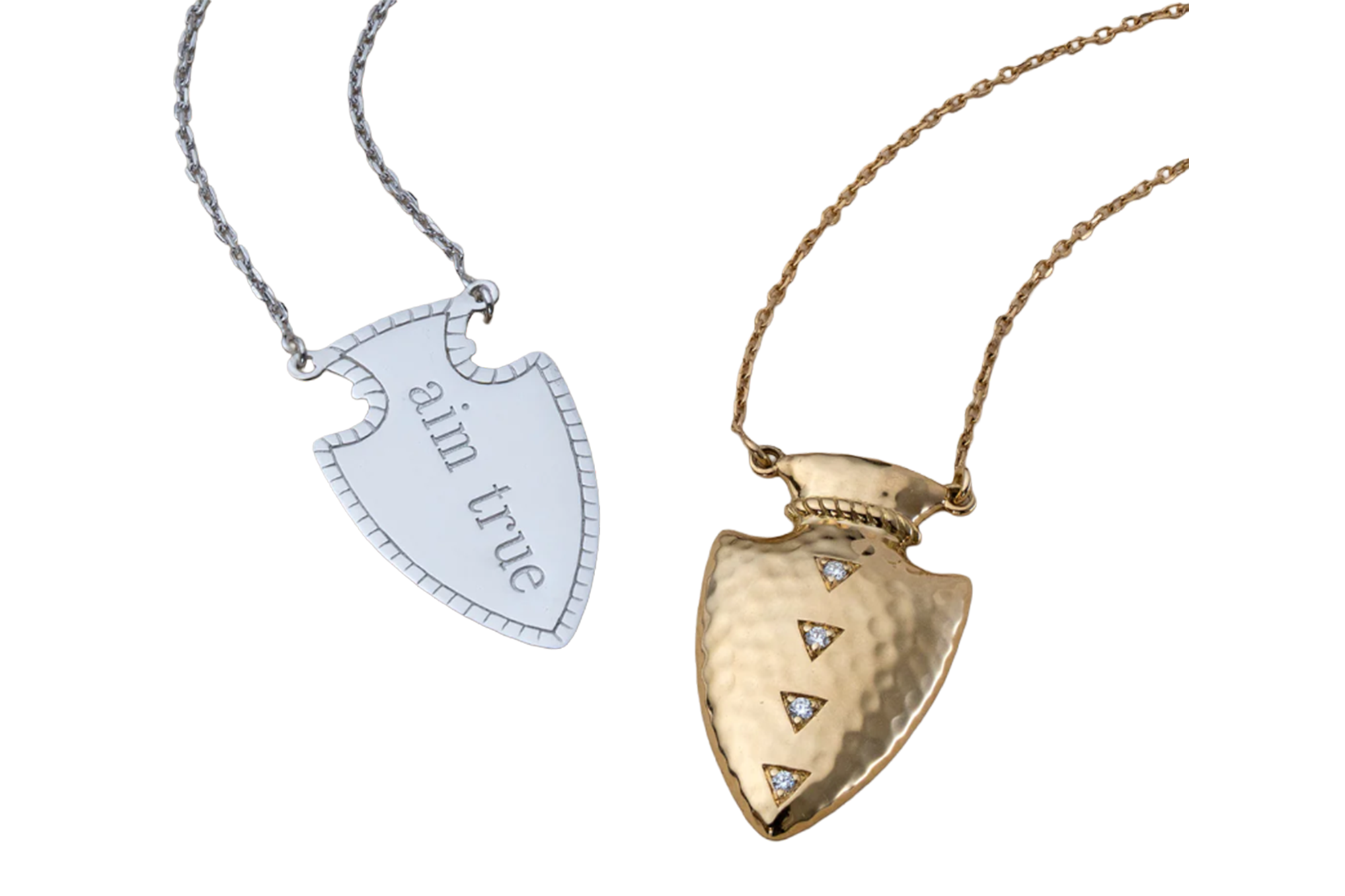 Two arrow-shaped pendants, one silver with "aim true" engraved, and one gold with three small diamonds.