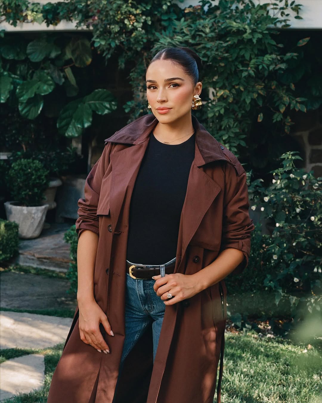 Olivia Culpo wearing a brown trench coat, black top, and jeans for an Abercrombie campaign.