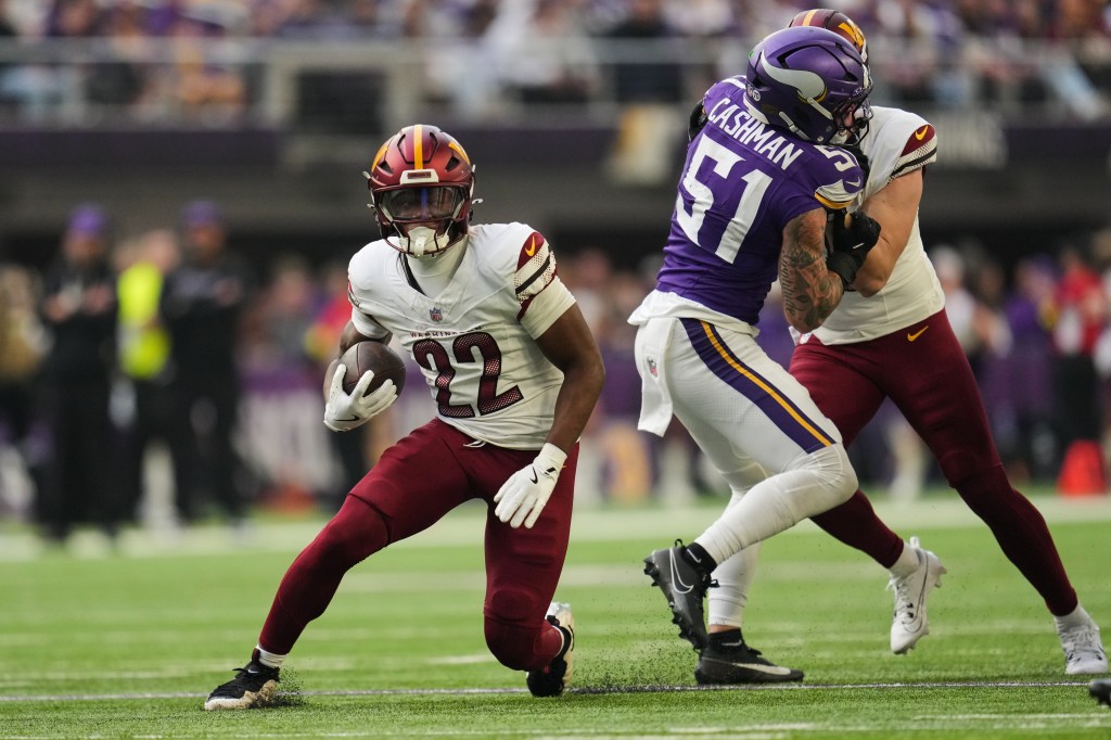Washington Commanders running back Jacory Croskey-Merritt (22) runs with the ball while being pursued by Minnesota Vikings player Cashman (51) during a football game.