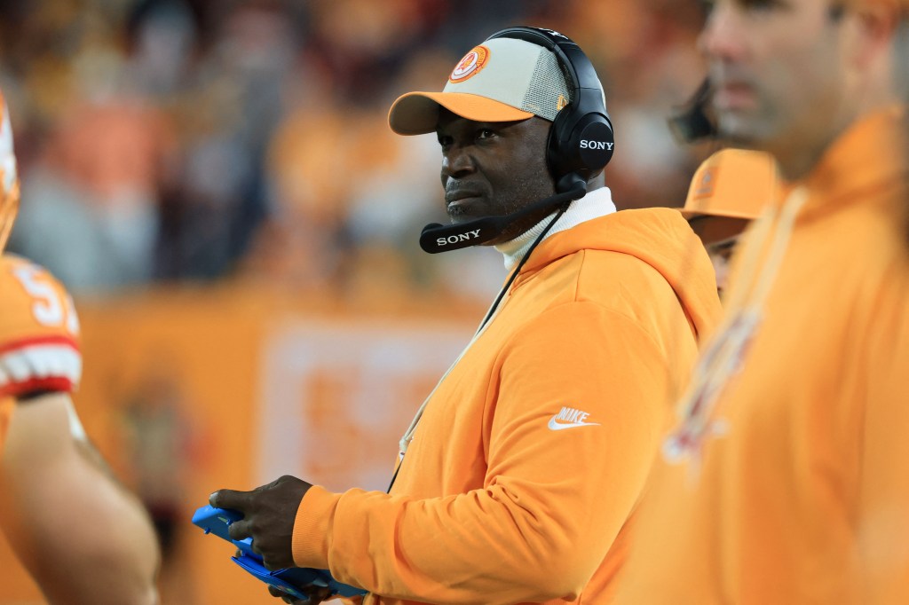 Todd Bowles in a white and orange hat and orange sweatshirt watching game play.