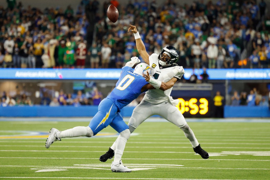 Philadelphia Eagles quarterback Jalen Hurts throws a football while being tackled by Los Angeles Chargers linebacker Daiyan Henley.