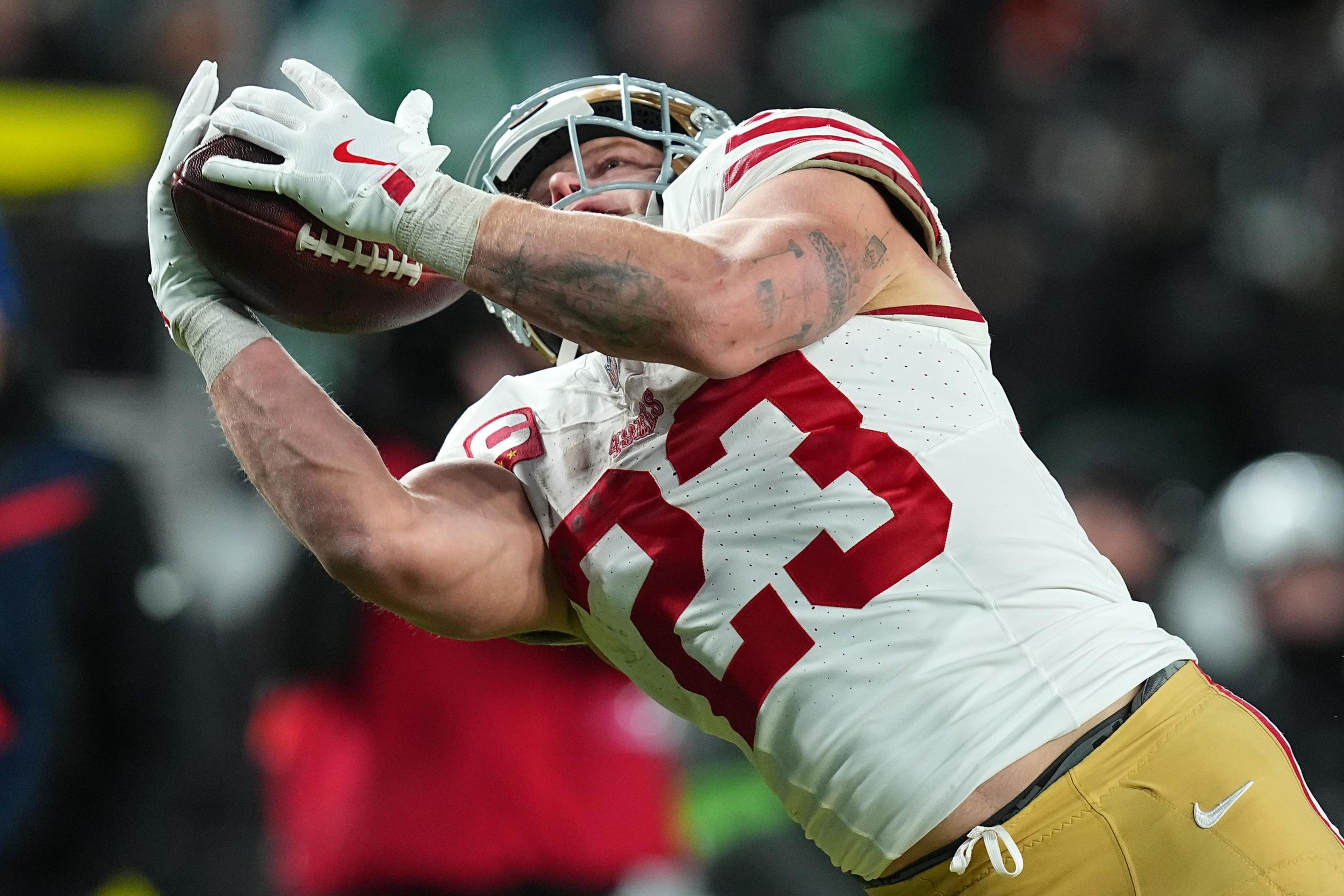 A football player wearing a white and red jersey with number 83 is stretching out arms to catch a football mid-air.