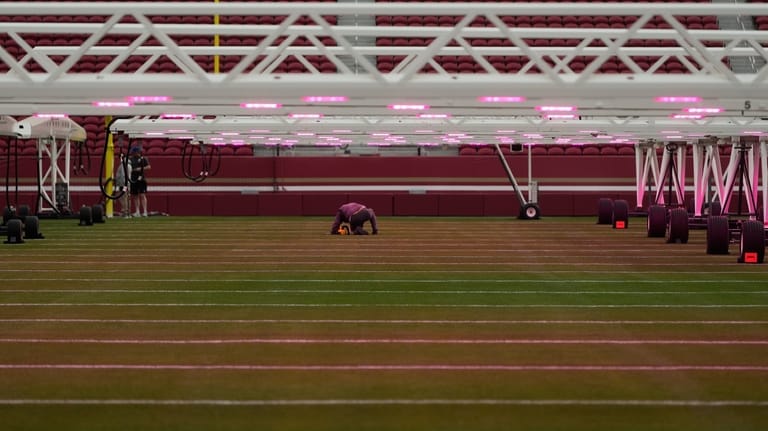 A worker kneels under grow lights on the field at...