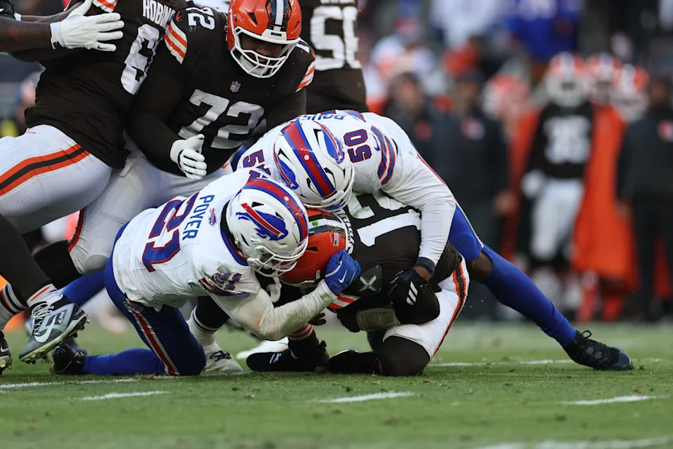 Dec 21, 2025; Cleveland, Ohio, USA; Cleveland Browns quarterback Shedeur Sanders (12) is sacked by Buffalo Bills safety Jordan Poyer (21) and defensive end Greg Rousseau (50) during the second half at Huntington Bank Field. Mandatory Credit: Scott Galvin-Imagn Images