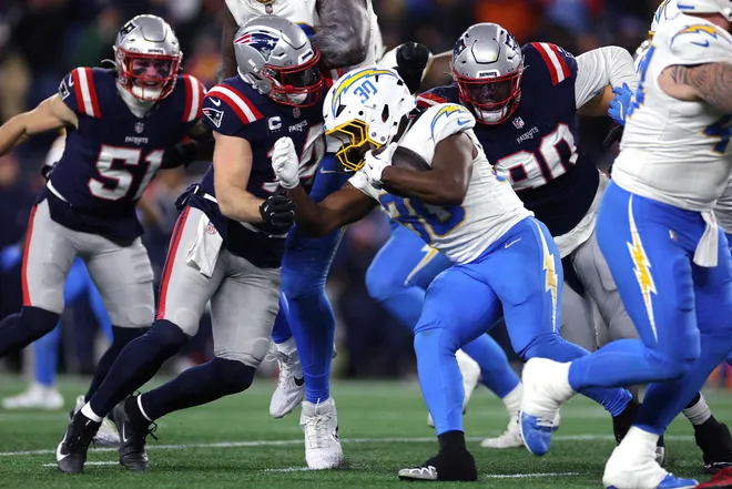 FOXBOROUGH, MASSACHUSETTS - JANUARY 11: Kimani Vidal #30 of the Los Angeles Chargers carries the ball defended by Robert Spillane #14 and Christian Barmore #90 of the New England Patriots during the third quarter of the AFC Wild Card Playoff game at Gillette Stadium on January 11, 2026 in Foxborough, Massachusetts. (Photo by Sarah Stier/Getty Images)