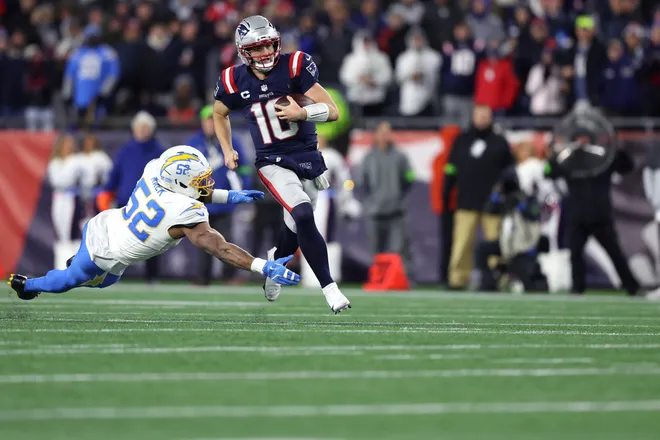 FOXBOROUGH, MASSACHUSETTS - JANUARY 11: Drake Maye #10 of the New England Patriots scrambles with the ball defended by Khalil Mack #52 of the Los Angeles Chargers during the third quarter of the AFC Wild Card Playoff game at Gillette Stadium on January 11, 2026 in Foxborough, Massachusetts. (Photo by Adam Glanzman/Getty Images)