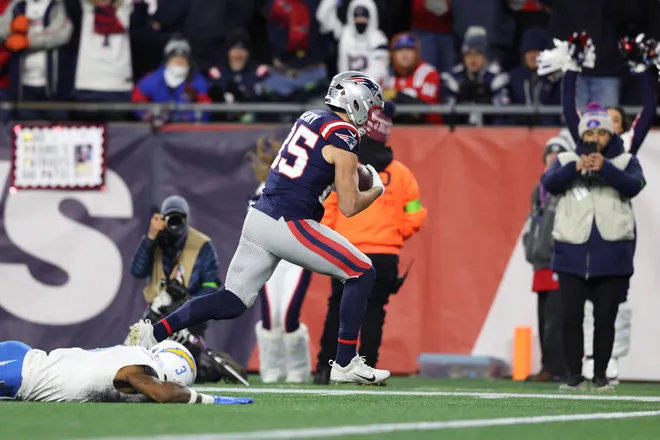FOXBOROUGH, MASSACHUSETTS - JANUARY 11: Hunter Henry #85 of the New England Patriots carries the ball after a reception for a touchdown defended by Derwin James Jr. #3 of the Los Angeles Chargers during the fourth quarter of the AFC Wild Card Playoff game at Gillette Stadium on January 11, 2026 in Foxborough, Massachusetts. (Photo by Adam Glanzman/Getty Images)
