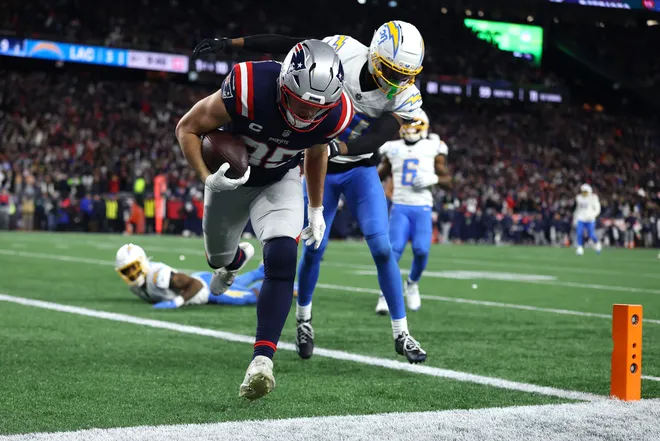 FOXBOROUGH, MASSACHUSETTS - JANUARY 11: Hunter Henry #85 of the New England Patriots carries the ball after a reception for a touchdown defended by Cam Hart #20 of the Los Angeles Chargers during the fourth quarter of the AFC Wild Card Playoff game at Gillette Stadium on January 11, 2026 in Foxborough, Massachusetts. (Photo by Sarah Stier/Getty Images)