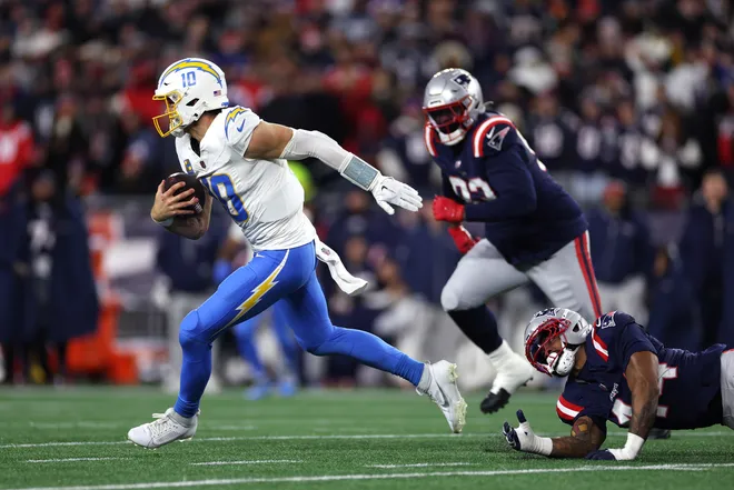 FOXBOROUGH, MASSACHUSETTS - JANUARY 11: Justin Herbert #10 of the Los Angeles Chargers avoids a tackle K'lavon Chaisson #44 of the New England Patriots during the second half of the AFC Wild Card Playoff game at Gillette Stadium on January 11, 2026 in Foxborough, Massachusetts. (Photo by Sarah Stier/Getty Images)
