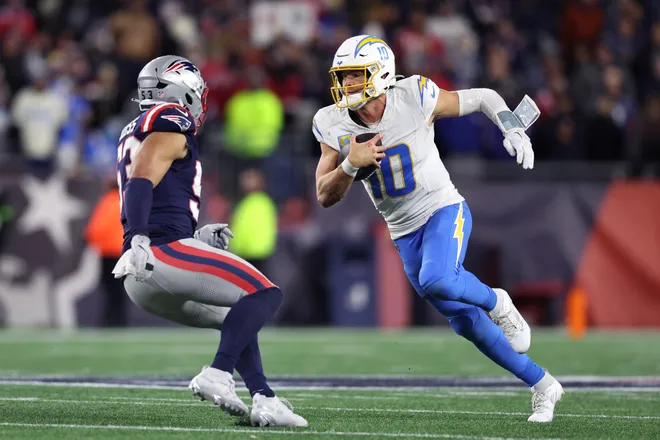 FOXBOROUGH, MASSACHUSETTS - JANUARY 11: Justin Herbert #10 of the Los Angeles Chargers scrambles with the ball defended by Christian Elliss #53 of the New England Patriots during the fourth quarter of the AFC Wild Card Playoff game at Gillette Stadium on January 11, 2026 in Foxborough, Massachusetts. (Photo by Adam Glanzman/Getty Images)