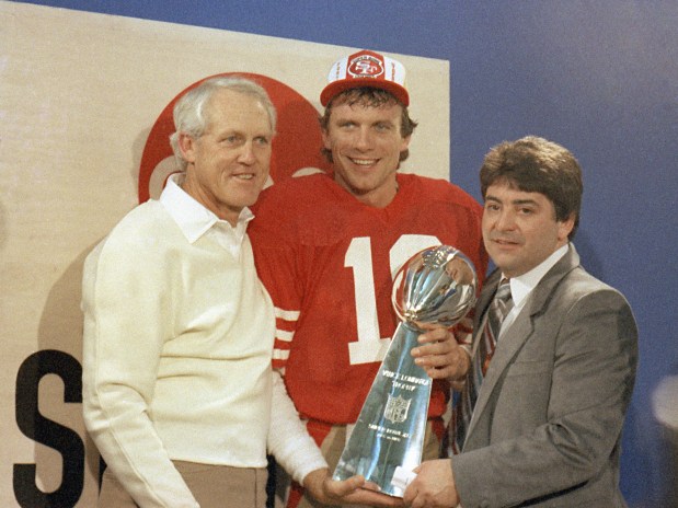 San Francisco 49ers' quarterback Joe Montana, center, is shown holding the Lombardi Super Bowl trophy with coach Bill Walsh, left, and 49ers' owner Edward DeBartolo, Jr., in the locker room at Palo Alto, Calif., Jan. 20, 1985.  (AP Photo)