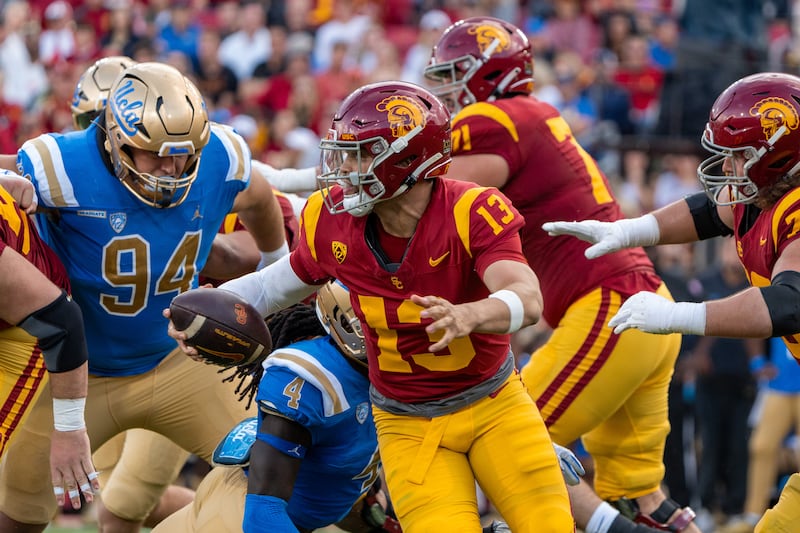 Caleb Williams (13) holds the football in his right hand and scrambles. Other USC and UCLA football players can be seen blocking in the background.