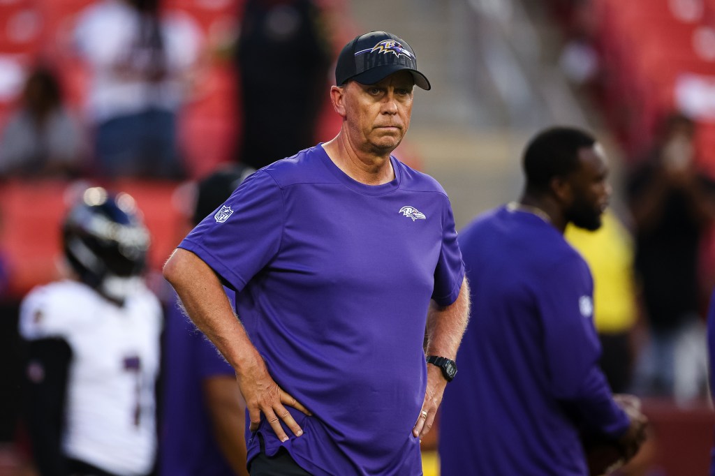 Baltimore Ravens coach in a purple shirt and black hat looking serious.