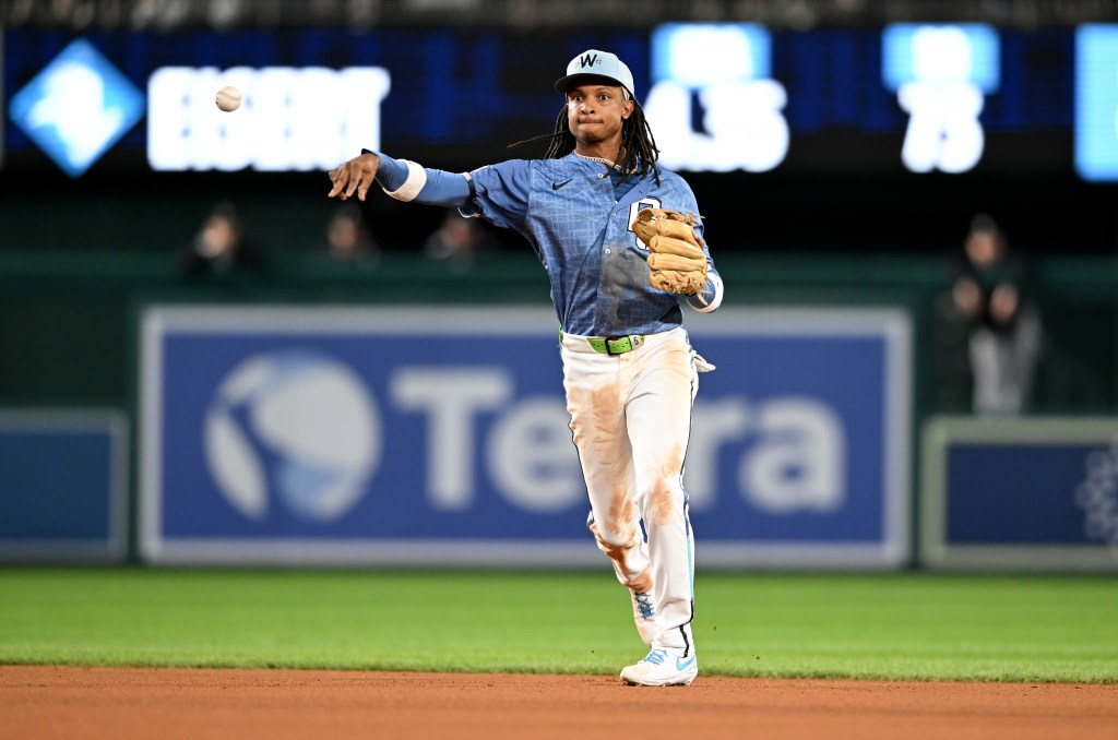 A baseball player in a light blue jersey and white pants with dirt stains throws a baseball.