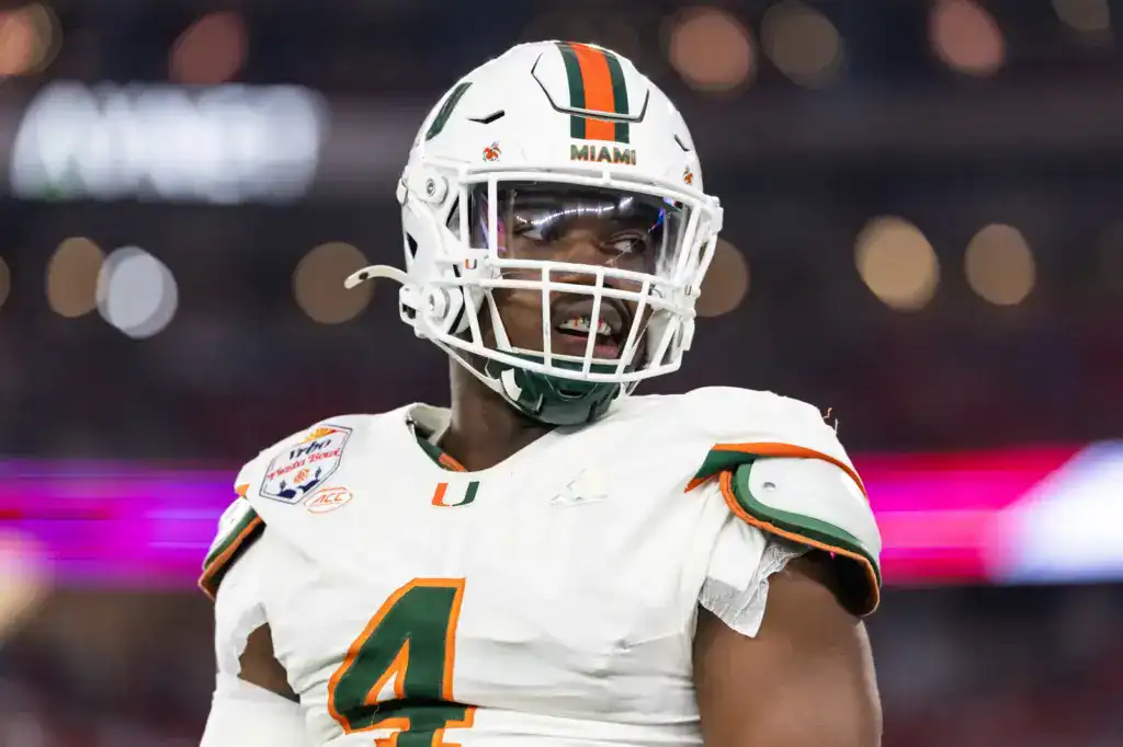 Miami Hurricanes defensive lineman, Rueben Bain Jr., wearing a white uniform with number 4, helmet on, looking to the side during a night game with stadium lights blurred in the background.