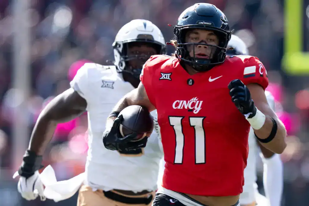 Cincinnati Bearcats linebacker, Jake Golday, wearing a red No. 11 jersey sprints upfield with the football as a offensive player gives chase.