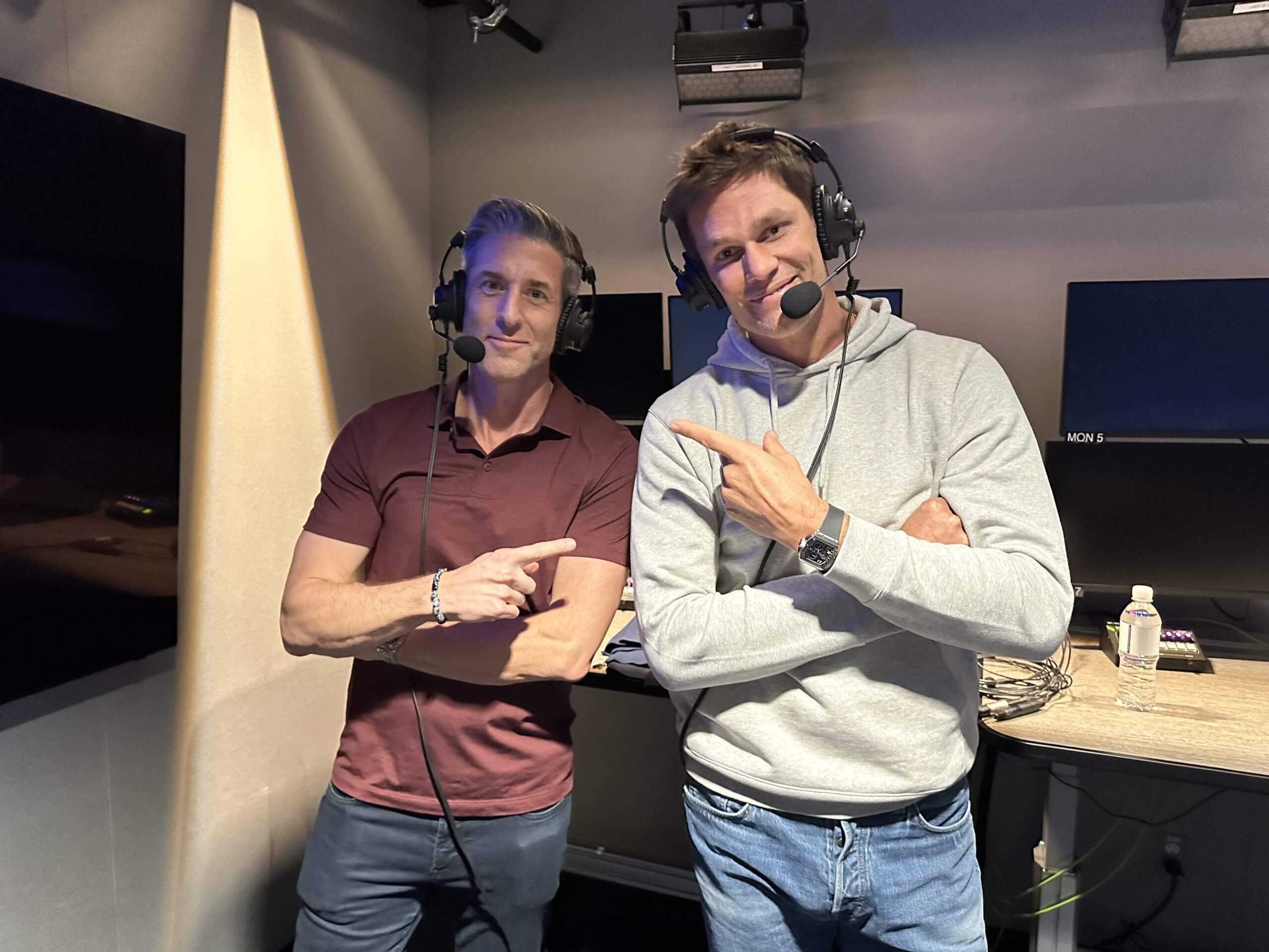 Kevin Burkhardt and Tom Brady stand in the broadcast studio together.